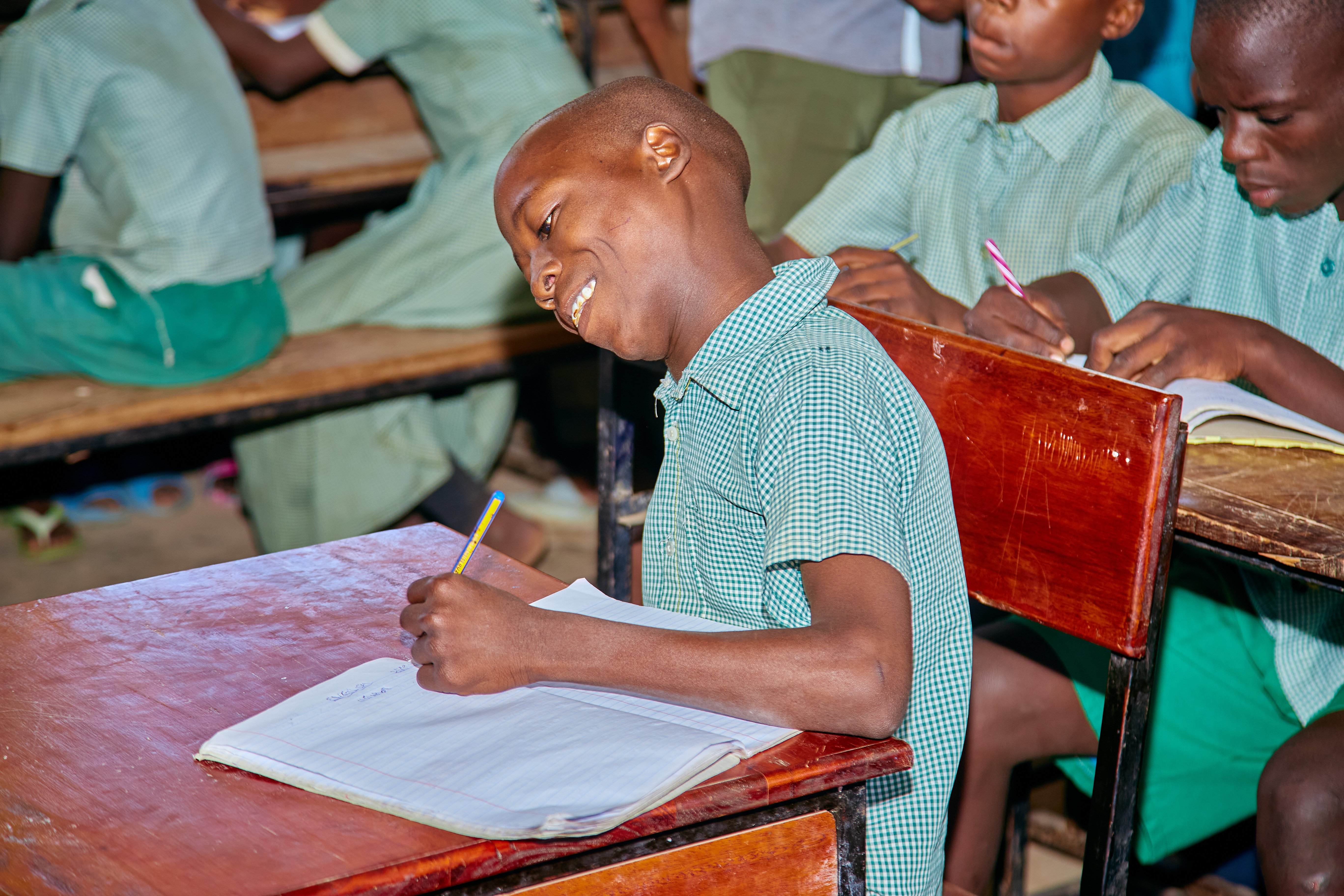 a boy smiles and writes in his notebook in the classroom 