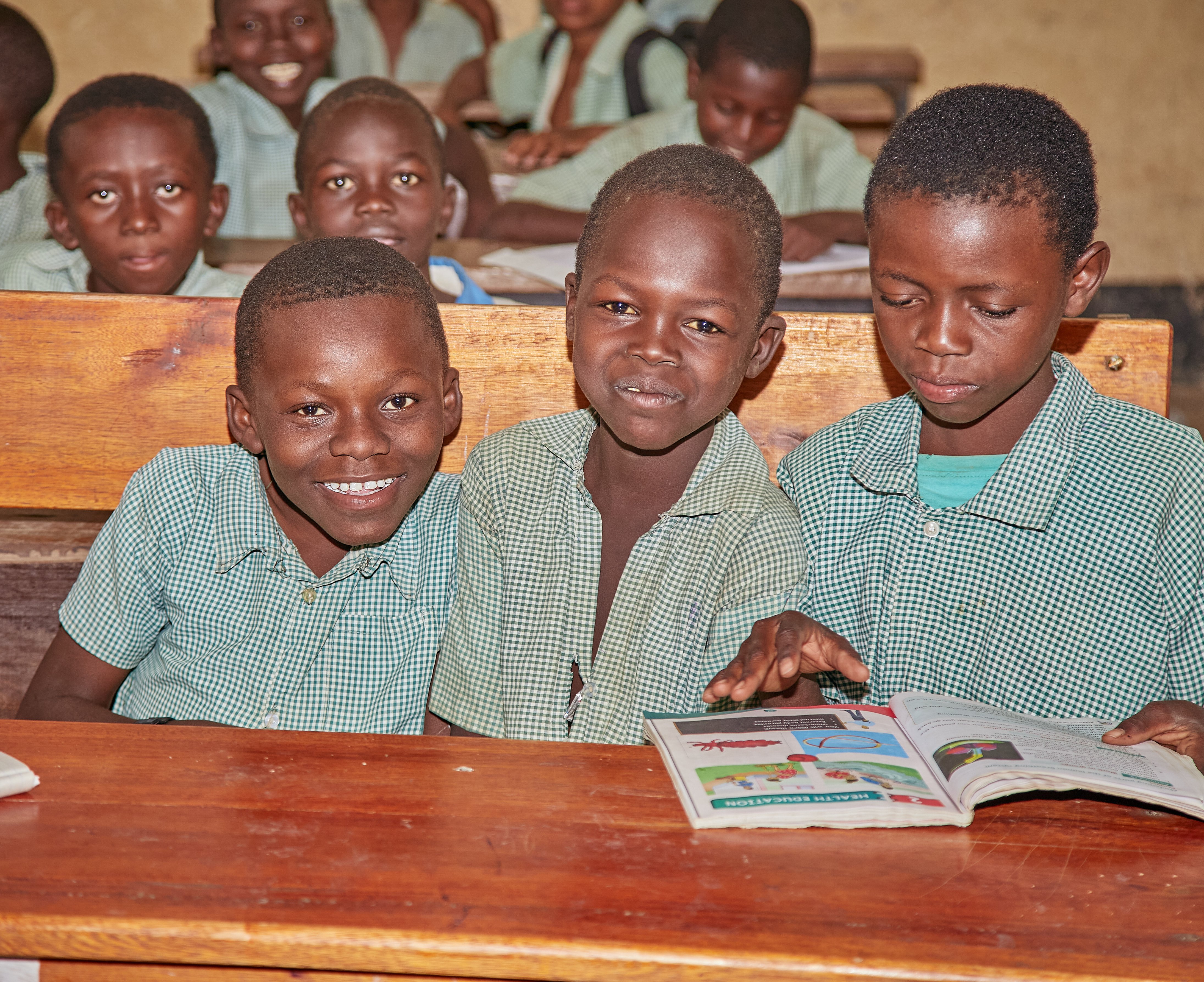 three boys sit next to each other in the classroom and grin into the camera 