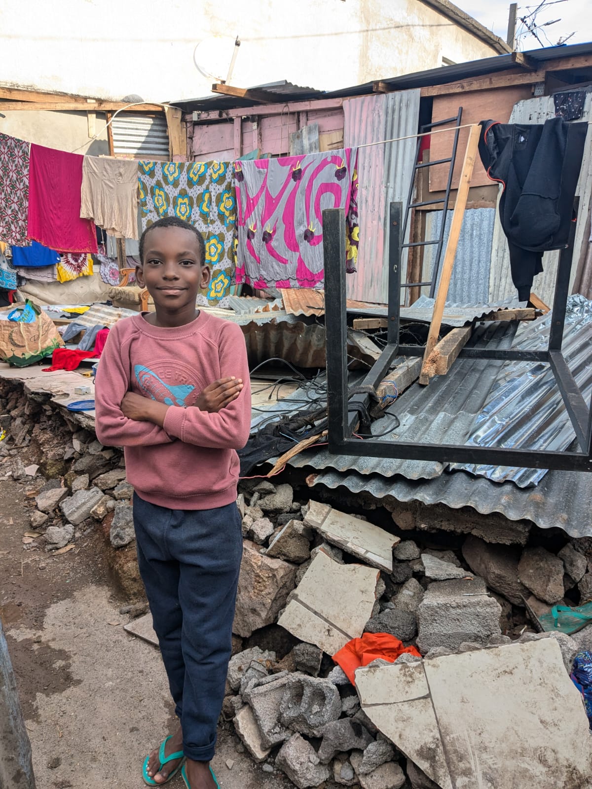 A young boy stands in front of his destroyed house