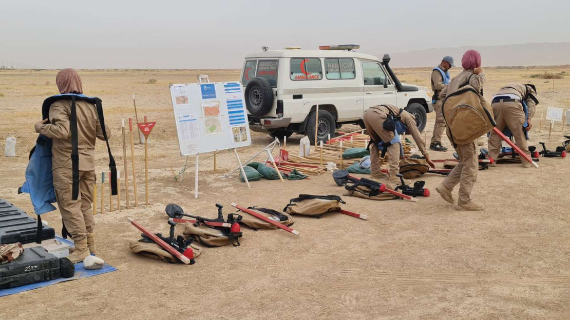 Demining team with their equipment, preparing to leave to clear an area. The team is in a seemingly deserted area. 