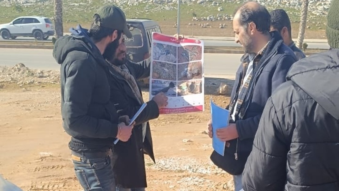 HI teams show two men a poster with different examples of unexploded ordnance found in Syria. 